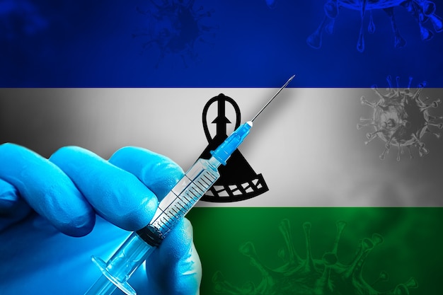 Campagna di vaccinazione LesothoCovid19 La mano in un guanto di gomma blu tiene la siringa davanti alla bandiera