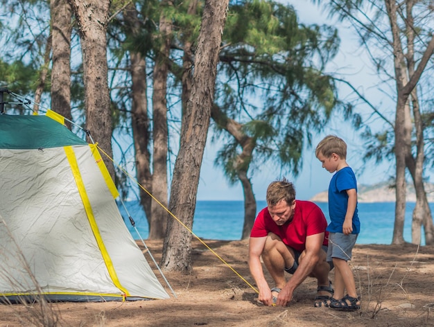 Campeggio persone all'aperto stile di vita turisti allestito verde grigio campeggio estate foresta vicino al mare di Lazur Ragazzo figlio aiuta il padre a studiare il meccanismo della moderna tenda facile da piegare Educazione naturale dei bambini