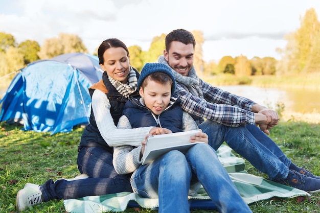 campeggio, turismo, escursione, tecnologia e concetto di persone - famiglia felice con computer tablet pc e tenda al campeggio