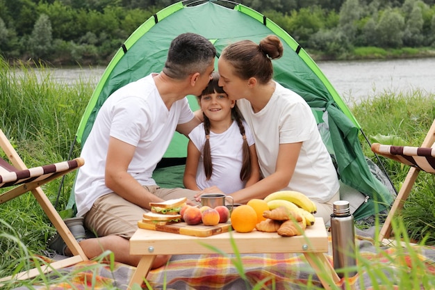 Campeggio vicino al fiume nel parco naturale Famiglia in vacanza Coppia con figlia a riposo Genitori che baciano la figlia Persone che si godono le vacanze