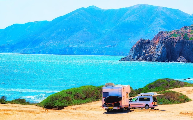 Camper e moto su strada a Capo Pecora al Mar Mediterraneo in Sardegna, Italia estate. Caravan camper e scooter in vacanza in autostrada. Minivan camper in autostrada. Cagliari. Tecnica mista.