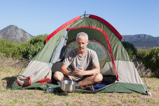 Camper felice che tiene tazza fuori della sua tenda