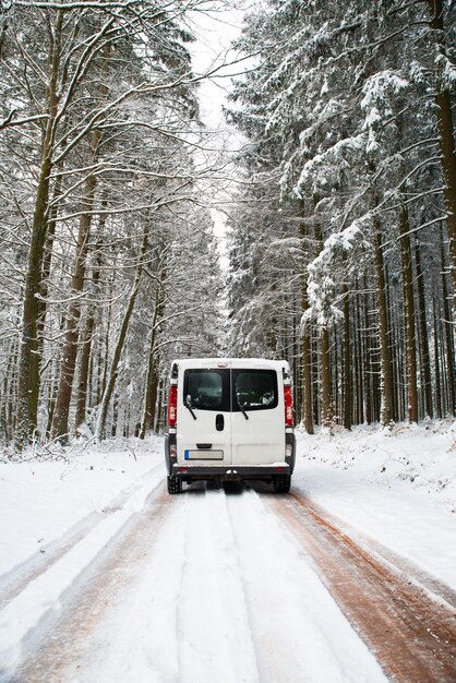 Camper Van che guida su una strada attraverso una foresta coperta di neve in inverno stile di vita di vacanza avventura