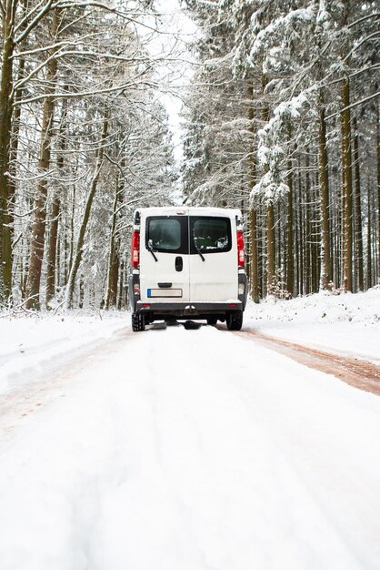 Camper Van che guida su una strada attraverso una foresta coperta di neve in inverno vacanza di avventura e stile di vita