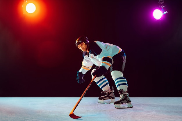 Campione. Giocatore di hockey maschio sul campo da ghiaccio e sfondo colorato al neon scuro con torce elettriche. Sportivo in attrezzatura, pratica del casco. Concetto di sport, stile di vita sano, movimento, benessere, azione.