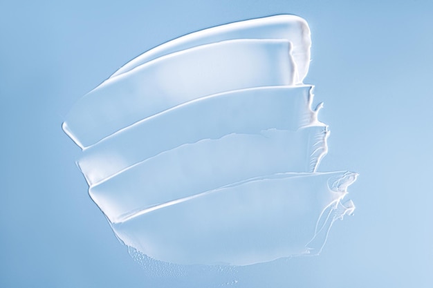 Campioni di sbavature bianche striscio di crema per la cura del viso o del corpo su sfondo blu Concetto di purezza