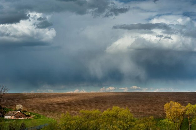 Campo coltivato all'inizio della primavera e terra e cielo abbandonati della fattoria con drammatiche nuvole temporalesche