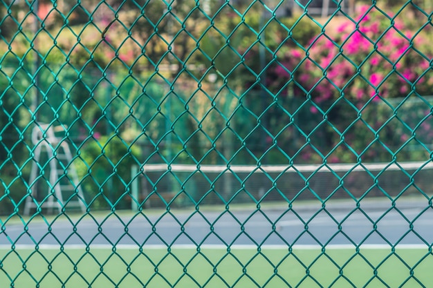 Campo da tennis vuoto nella moderna torre dell'hotel di moda per la vista dell'arbitro attraverso la recinzione in rete metallica Colori verdi tropicali freschi luminosi Sport divertimento vacanze estive attività di stile di vita all'aperto Giornata di sole