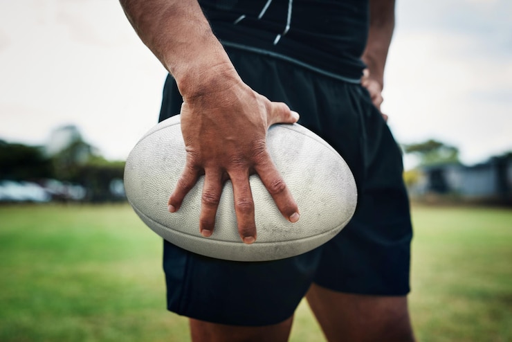 Foto campo di rugby e mani dell'uomo con la palla nello stadio per la competizione di allenamento della partita e il gioco giocatore di primo piano e atleta maschio sull'erba pronti per l'allenamento di abilità sportive all'aperto o esercizio fisico