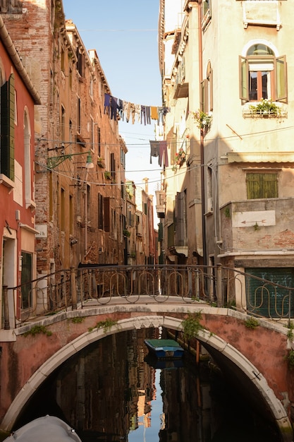 Canale a Venezia italiana tra antichi edifici con barche su di esso. E un ponte pedonale attraverso questo ponte.