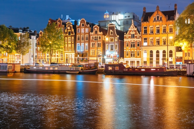 Canale di Amsterdam Amstel con tipiche case olandesi, casa galleggiante e pista luminosa dalla barca di notte, Olanda, Paesi Bassi.