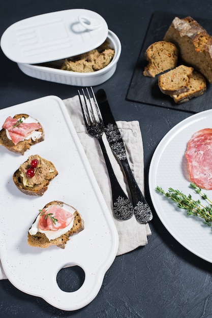 Canape con prosciutto, salame e paté d&#39;anatra su un tagliere bianco &amp;