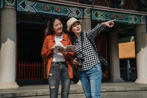 Cancello del padiglione cinese sullo sfondo. giovani ragazze viaggiatori che visitano la storia di Pechino tempio di Confucio cina libro guida hodling discutendo di informazioni. turisti femminili puntano il dito mostrando.