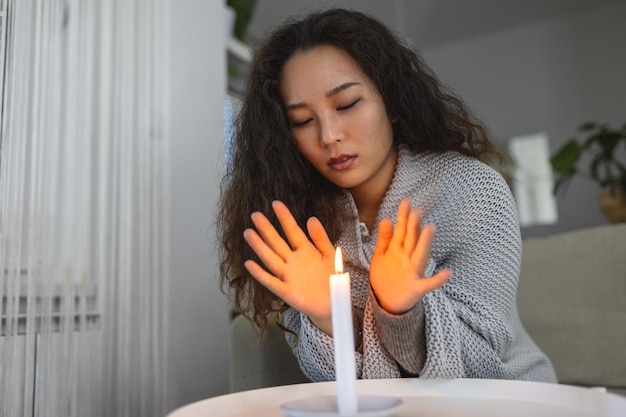 Candela accesa donne che cercano di riscaldarsi le mani in casa buia Arresto del riscaldamento e interruzione di corrente elettrica blackout perdita di carico o crisi energetica