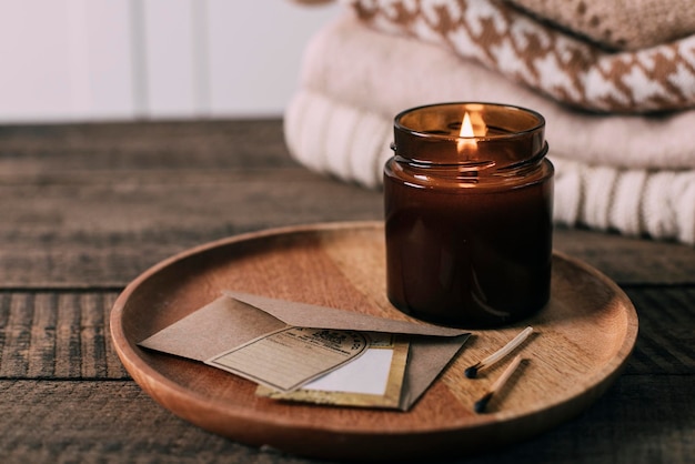 Candela accesa in vasetto di vetro ambrato con pile di stoppino in legno maglioni stagionali a maglia Accogliente stile di vita