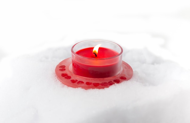 Candela bruciante rossa di Natale nel candeliere di vetro trasparente sul fondo della neve