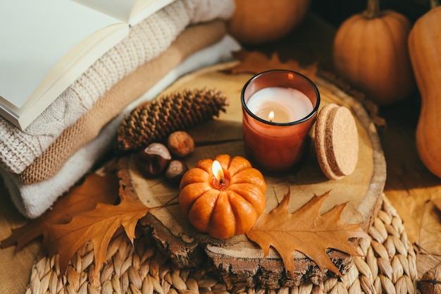 Candela bruciante zucca e una tazza di tè sullo sfondo di una pila di maglioni composizione autunnale