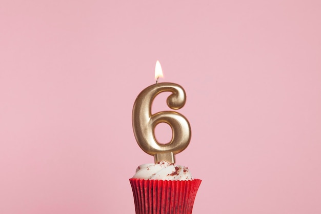 Candela d'oro numero 6 in un cupcake su uno sfondo rosa pastello