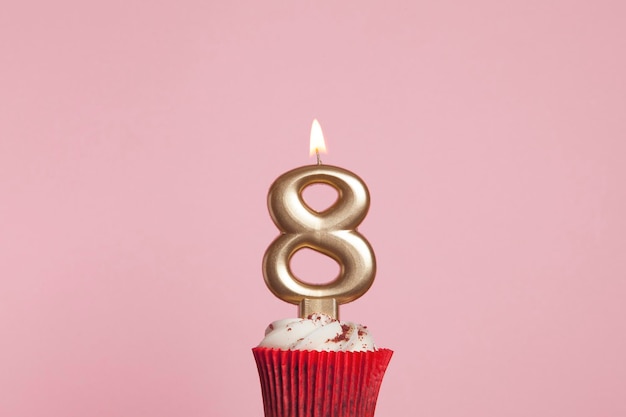 Candela d'oro numero 8 in un cupcake su uno sfondo rosa pastello