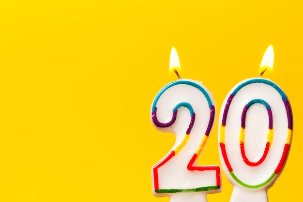 Candela di celebrazione di compleanno numero 20 su uno sfondo giallo brillante