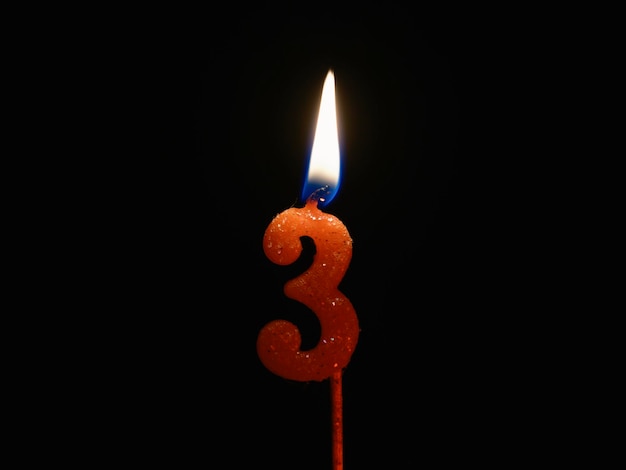 Candela di compleanno accesa isolata su sfondo nero numero 3