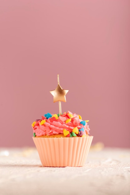 Candela festiva delle stelle sopra i bigné. Muffin glassato con glassa al burro rosa su sfondo rosa. Cornice verticale