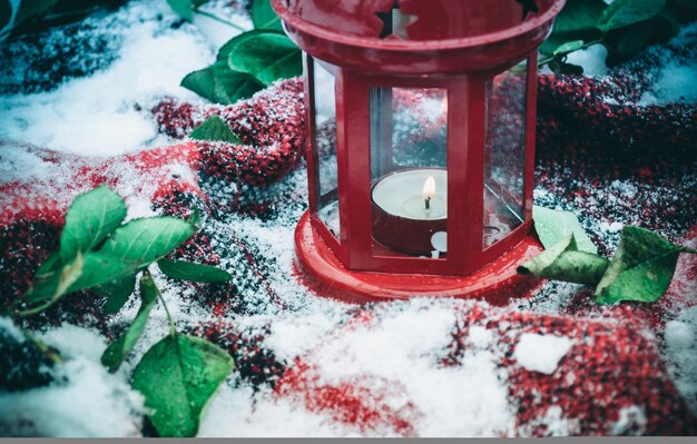 Candela rossa festiva in lanterna e tazza di caffè su tappeto con neve