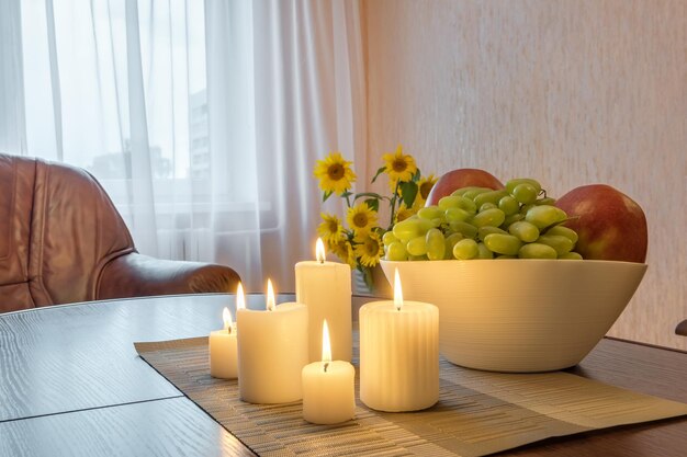 Candele accese e un vaso con mele da frutta e uva sul tavolo vicino alla lampada