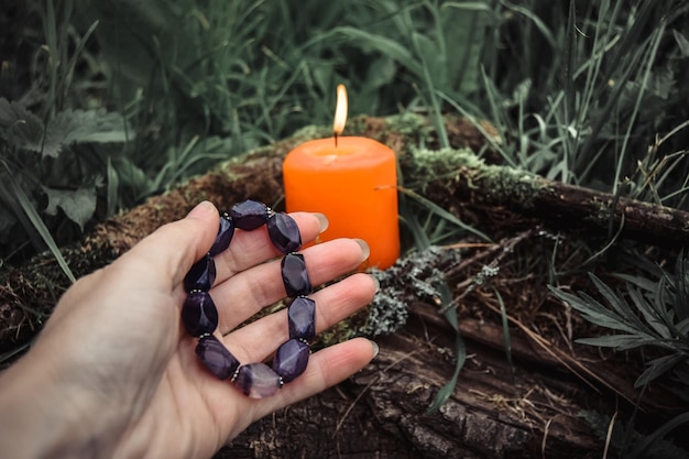 Candele accese e una mano di donna con un braccialetto su uno sfondo naturale scuro pagan wiccan tradizioni slave stregoneria rituale spirituale esoterico per mabon halloween samhain festival dell'equinozio d'autunno