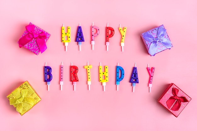 Candele colorate sulla torta a forma di lettere buon compleanno sul rosa