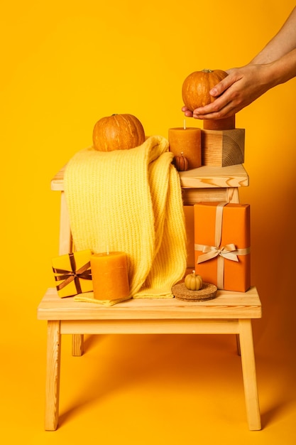 Candele e maglione su mensole di legno e zucca in mani femminili su sfondo giallo