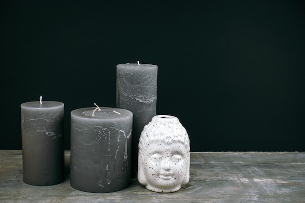 Candele grigie e testa di Buddha in ceramica bianca su un tavolo di fronte al muro nero