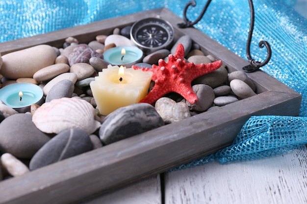 Candele su vassoio vintage con ciottoli di mare, stelle marine e conchiglie su fondo di legno