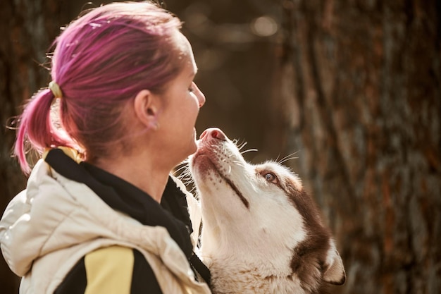 Cane Husky siberiano che bacia una donna con i capelli rosa, il vero amore per l'uomo e l'animale domestico divertente si incontrano