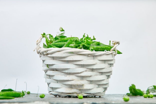 Canestro bianco con i piselli freschi su fondo grigio.