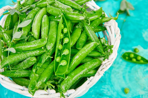 Canestro bianco con i piselli freschi sulla tavola blu. Concetto di cibo vegano e vegetariano. Disteso.