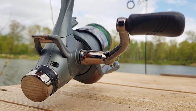 Canna da pesca alla carpa isolata sul lago e sul ponte di legno. Bobina di filatura dell'alimentatore della carpa da vicino. Pesca alla carpa sul lago. Attrezzatura del pescatore.