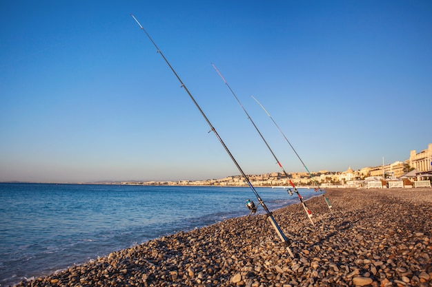 Canne da pesca su una spiaggia di ciottoli sulla Promenade des Anglais all'alba, Nizza, Francia