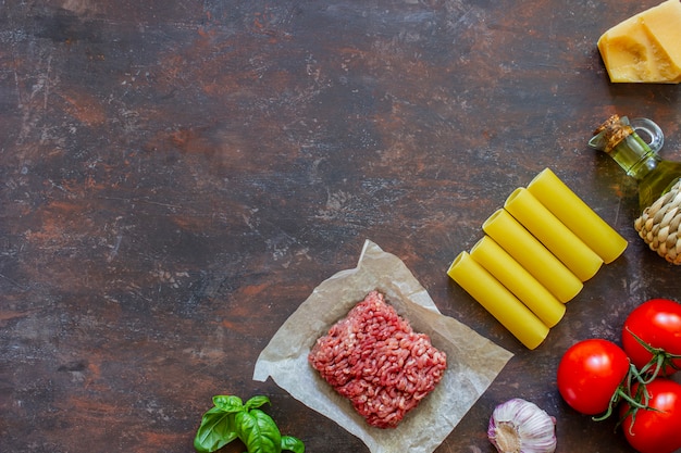 Cannelloni, pomodori, carne macinata e altri ingredienti. Sfondo scuro Cucina italiana.