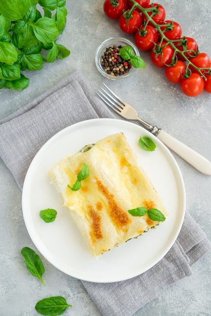 Cannelloni tradizionali italiani con ricotta e spinaci in salsa besciamella con foglie di basilico fresco