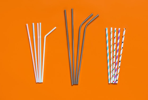 Cannucce riutilizzabili in carta e acciaio come sostituto alternativo per cannucce in plastica su sfondo arancione vista dall'alto