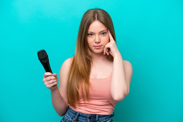 Cantante donna caucasica che prende un microfono isolato su sfondo blu pensando un'idea