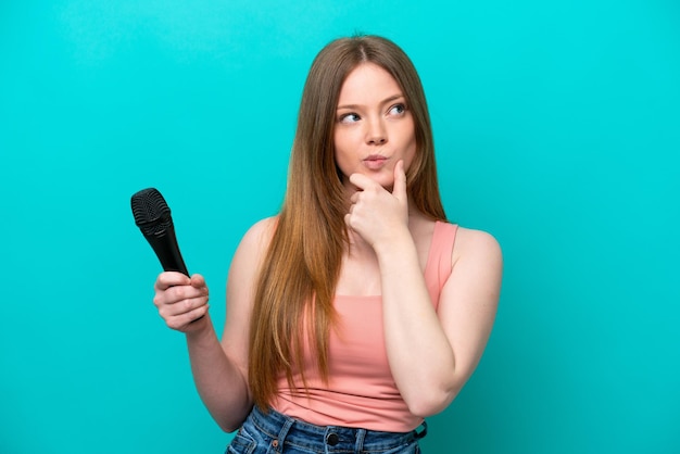 Cantante donna caucasica che raccoglie un microfono isolato su sfondo blu con dubbi e pensare