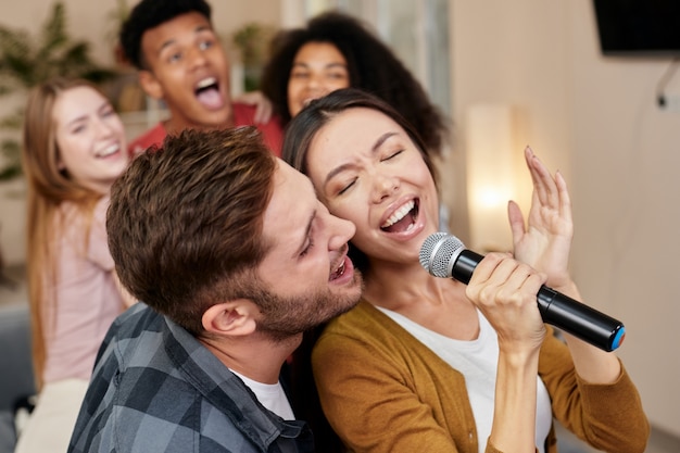 Cantate insieme giovani coppie o amici eccitati che tengono il microfono e cantano insieme mentre suonano