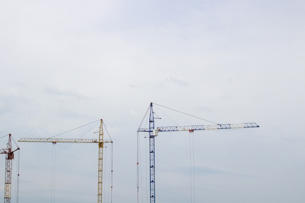 Cantiere con gru alte contro il cielo blu. Un edificio residenziale è in costruzione.