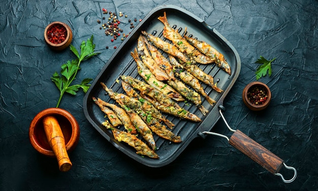 Capelin fritto guarnito con prezzemolo e scorza di limone in padella