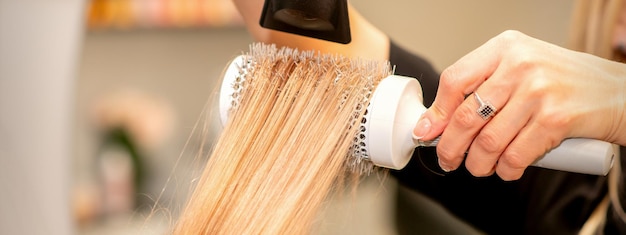 Capelli asciutti del parrucchiere professionista con un asciugacapelli e una spazzola per capelli rotonda in un salone di bellezza.