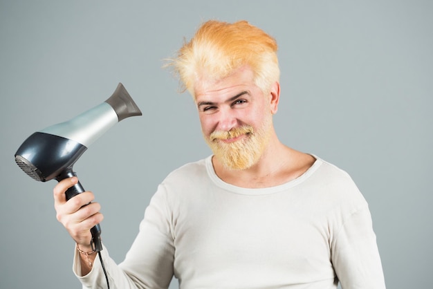 Capelli biondi dell'uomo barbuto asciutti. Giovane uomo che asciuga i capelli con l'asciugacapelli.