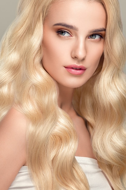 Capelli biondi Donna Bella acconciatura riccia Capelli lunghi ondulati Naturale Compongono. Colpo dello studio. su grigio