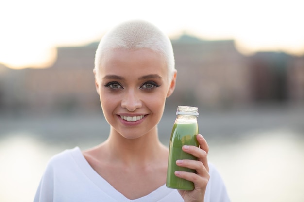 Capelli corti biondi della giovane donna millenario all'aperto con il frullato verde